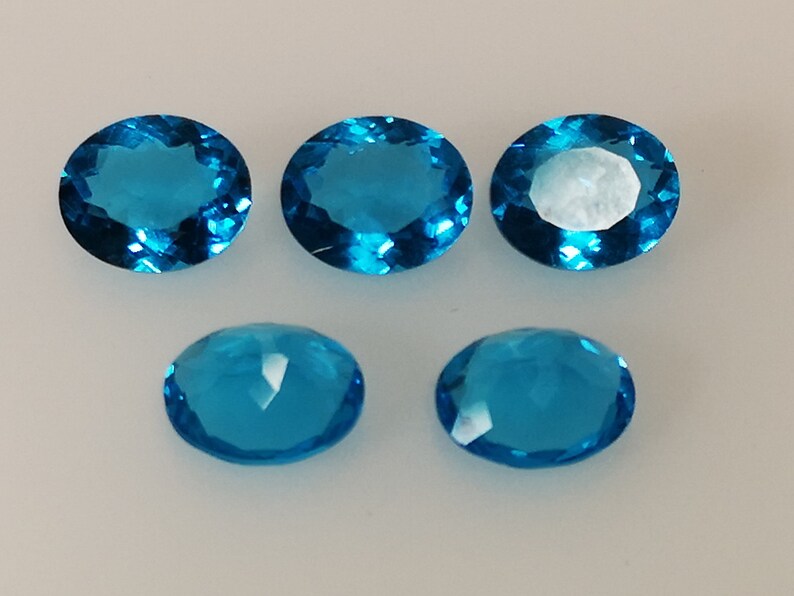 May include: Six oval-shaped, faceted, blue gemstones. The gemstones are arranged in two rows of three.