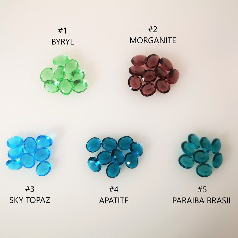 May include: A collection of ten oval-shaped gemstones in five different colours. The gemstones are labelled #1 Byryl, #2 Morganite, #3 Sky Topaz, #4 Apatite, and #5 Paraiba Brasil.