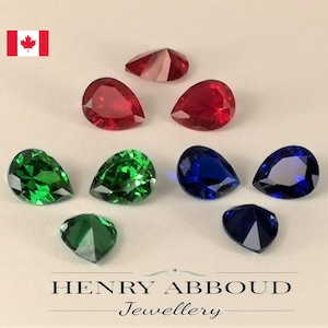 May include: Assortment of pear-shaped gemstones in red, green, and blue colours. The gemstones are arranged on a white surface.