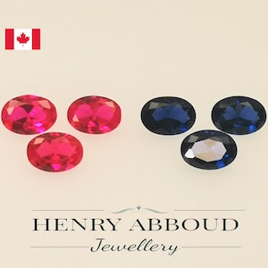 May include: Three oval-shaped red gemstones and three oval-shaped blue gemstones. The gemstones are arranged in two rows, with the red gemstones on top and the blue gemstones on the bottom. The gemstones are on a white background. Henry Abboud Jewellery.