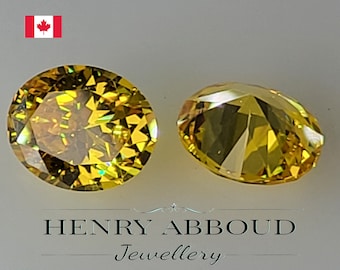 May include: Two yellow oval-shaped gemstones with a faceted cut. The gemstones are on a white surface.