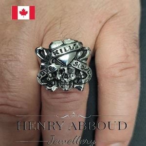 May include: A silver ring with a skull and crossbones design. The skull has black eyes and the ring has the words "Love Kills Slowly" inscribed on it.