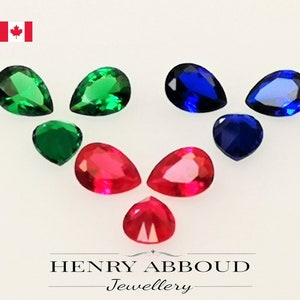 May include: Assortment of pear-shaped gemstones in red, green, and blue. The gemstones are arranged in a pattern on a white surface.  Henry Abboud Jewellery.