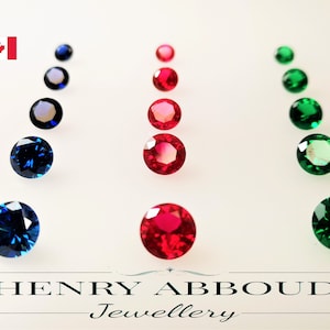 Peut inclure: Une collection de pierres précieuses rondes de différentes tailles, y compris du bleu, du rouge et du vert. Les pierres précieuses sont disposées en rangées sur une surface blanche. L'image comprend le texte "HENRY ABBOUD Jewellery".