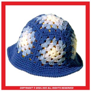 Op de afbeelding: Een blauwe gehaakte hoed met een wit en lichtblauw granny square patroon.