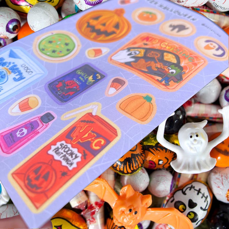 May include: A sheet of Halloween-themed stickers featuring pumpkins, candy corn, and spooky beverages. The stickers are on a light purple background with a spiderweb design. The words "Spooky Fruit Punch" are visible on one sticker.