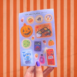 May include: A sheet of Halloween-themed stickers with various designs, including pumpkins, ghosts, and candy corn. The text "Y2K Halloween" is at the top. The stickers are on a purple background with an orange and white striped background.