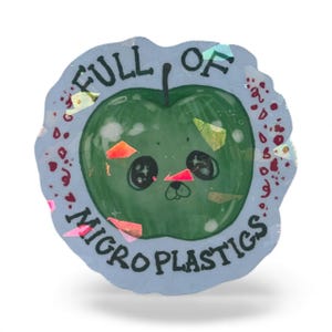 May include: A round sticker with a green apple illustration and the text "FULL OF MICROPLASTICS". The apple has a cute face and is surrounded by colorful confetti-like shapes. The sticker has a light blue border.