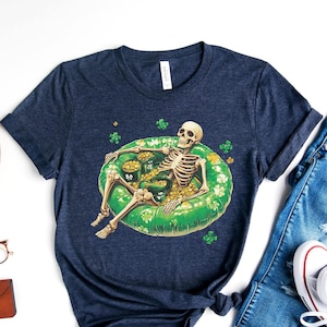May include: A navy blue t-shirt with a skeleton wearing a green inflatable ring and holding gold coins. The skeleton is surrounded by shamrocks.