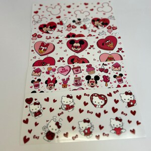 May include: A set of five Valentine's Day themed nail stickers featuring Mickey Mouse, Minnie Mouse, and Hello Kitty. The stickers are on a white background with red hearts and other Valentine's Day themed designs.