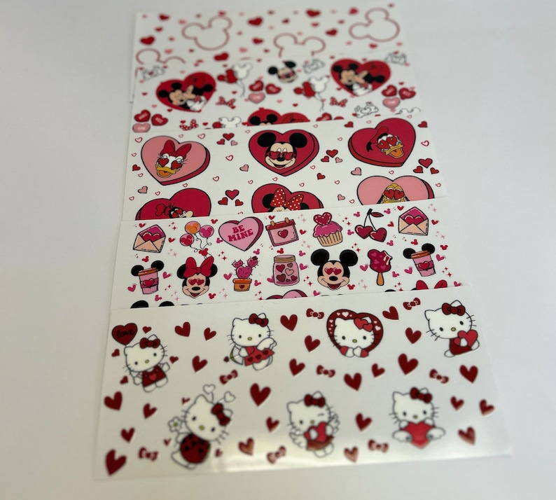 May include: A set of five Valentine's Day themed nail stickers featuring Mickey Mouse, Minnie Mouse, and Hello Kitty. The stickers are on a white background with red hearts and other Valentine's Day themed designs.