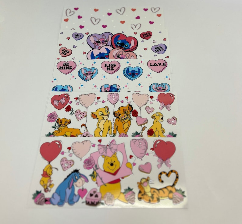 May include: A set of four Valentine's Day themed sticker sheets featuring Disney characters. The sheets feature Stitch, Simba, and Winnie the Pooh. The stickers are printed on clear sheets and have a variety of designs, including hearts, balloons, and candy.