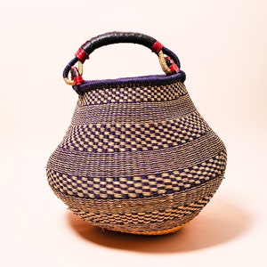 Puede incluir: Una cesta grande tejida con un patrón de color púrpura y paja natural. La cesta tiene un asa de cuero negro con detalles rojos.