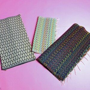 May include: Three woven mats with different patterns. The first mat is beige with a black diamond pattern. The second mat is white with a multi-colored chevron pattern. The third mat is black with a multi-colored chevron pattern.