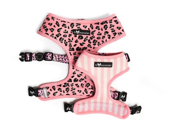 Puede incluir: Dos arneses rosas para perros. Uno presenta un estampado de leopardo con manchas negras, el otro tiene rayas verticales rosas y blancas. Ambos tienen hebillas negras y el logo "lil monster".