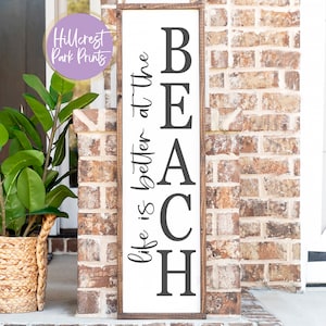 May include: A white wooden sign with black lettering that reads "Life is better at the BEACH". The sign is hanging on a brick wall.