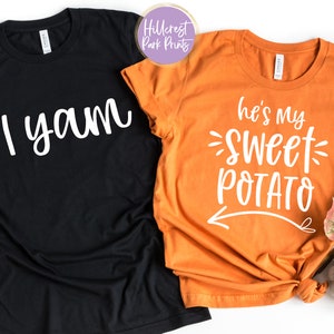 May include: Two t-shirts, one black and one orange. The black shirt has the text "I yam" in white script. The orange shirt says "he's my SWEET POTATO" in white script with an arrow pointing left. The shirts are likely for couples.
