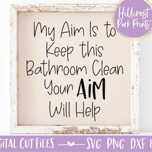 May include: A white framed sign with the text "My Aim Is to Keep this Bathroom Clean Your AiM Will Help" on a beige background.