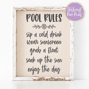 May include: A framed sign with the words "POOL RULES" in black script. The rules listed are "sip a cold drink, wear sunscreen, grab a float, soak up the sun, enjoy the day." The frame is white with a distressed finish.