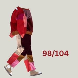 Könnte beinhalten: Ein Patchwork-Sweatshirt und -Hosen-Set in Rot-, Rosa-, Braun- und Beigetönen. Das Outfit hat ein Peace-Zeichen auf den Schuhen und die Zahl "98/104" in rotem Text.
