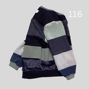Könnte beinhalten: Ein Patchwork-Sweatshirt in verschiedenen Blau-, Grün- und Grautönen. Das Design weist eine Mischung aus Texturen auf, darunter Samt und strukturiertes Gewebe. Die Zahl "116" ist sichtbar. Das Sweatshirt hat einen Rundhalsausschnitt und lange Ärmel.
