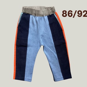 Könnte beinhalten: Farblich abgesetzte Hose in Hellblau, Marineblau und Orange. Die Hose hat einen beigen Gummibund und die Größe 86/92 ist oben rechts aufgedruckt. Die Hose hat eine lockere Passform.