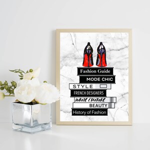 May include: A framed print with a white marble background featuring a pair of red-soled black high heels on top of a stack of books. The books have the titles "Fashion Guide", "Mode Chic", "Style", "French Designers", "Haute Couture", "Beauty", and "History of Fashion".