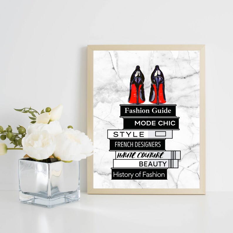May include: A framed print with a white marble background featuring a pair of red-soled black high heels on top of a stack of books. The books have the titles "Fashion Guide", "Mode Chic", "Style", "French Designers", "Haute Couture", "Beauty", and "History of Fashion".