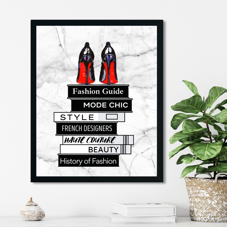 May include: Black and red high heels on top of a stack of books with the titles "Fashion Guide", "Mode Chic", "Style", "French Designers", "Haute Couture", "Beauty", and "History of Fashion". The books are on a white marble background.