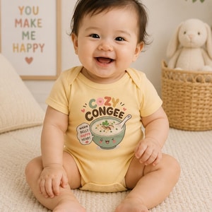 May include: A light yellow baby bodysuit featuring a graphic of a bowl of congee with a spoon. The text reads COZY CONGEE and WARM BELLY HAPPY HEART. The design includes small hearts and dots surrounding the bowl, which has a smiling face.