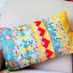 Könnte beinhalten: Dekoratives Kissen mit floralem und geometrischem Patchwork-Design. Das Kissen zeigt eine Kombination aus gelben, roten und blauen Stoffen. Im Hintergrund ist ein passender Wandbehang mit ähnlichen Mustern und Farben zu sehen.