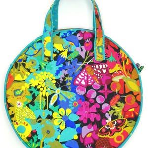Könnte beinhalten: Eine runde, türkisfarbene und schwarze Stofftasche mit einem bunten Blumen- und Schmetterlingsdruck. Die Tasche hat einen türkisfarbenen Henkel und einen Reißverschluss.