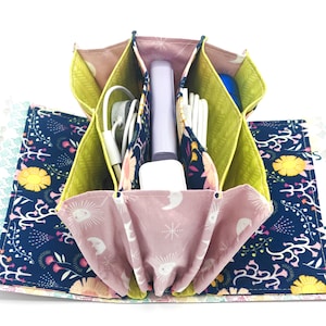 May include: Open, multi-compartment fabric organiser with a floral and celestial print. The interior compartments are lime green and hold various tech accessories. The exterior features a navy blue floral pattern and a pink fabric with moons and stars.