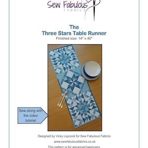 May include: A blue and white patchwork table runner with a three-star pattern. The table runner is 14 inches by 40 inches. The table runner is on a wooden table with two silver forks and a white plate.