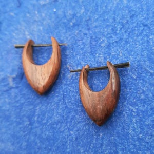 May include: A pair of wooden earrings with a dark brown colour and a unique teardrop shape. The earrings are made of wood and have a simple design.
