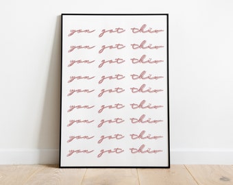 May include: A framed print with the phrase "you got this" repeated in a pink script font on a white background. The print is in a black frame and is displayed against a white wall and wooden floor.
