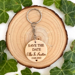 May include: A round wooden keychain with the text "Save the Date" and the names "Ellie & Austin" and the date "13.05.2022" engraved on it.