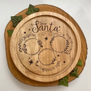 May include: Wooden serving tray with a festive design for Christmas. It has three circles for placing treats, with the text "Dear Santa", "For the Reindeer", "Our Favourite Cookies", and "Something to Drink".