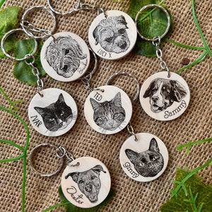 May include: Seven personalized pet keychains with engraved names and images of dogs and cats. The keychains are made of wood and have a silver metal ring.