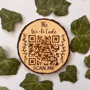 May include: A wooden round disc with the text "The Wi-Fi Code" and a QR code with the text "SCAN ME" below it. The disc is surrounded by green leaves.