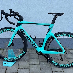 Könnte beinhalten: Ein türkisfarbenes und schwarzes Bianchi Rennrad mit schwarzen Rädern und einem schwarzen Lenker. Das Fahrrad hat ein schwarz-weißes Muster auf den Rädern.