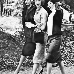 Könnte beinhalten: Drei Frauen in Schwarz-Weiß-Kleidung gehen in einem Park spazieren. Die Frau in der Mitte trägt einen gemusterten Rock und eine schwarze Handtasche. Die Frau links trägt einen langen schwarzen Mantel und die Frau rechts trägt einen weißen Schal.