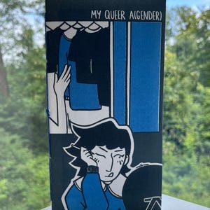 Op de afbeelding: Een stripachtige illustratie met de tekst "MY QUEER (AGENDER)". Het kunstwerk toont een persoon in een blauwe trui, die nadenkend kijkt, en een gestileerde kledingkastscène. Het kleurenpalet omvat blauw, zwart en wit.