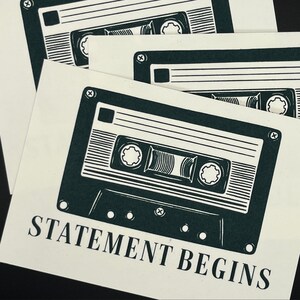 Könnte beinhalten: Mehrere cremefarbene Karten mit einem dunkelgrünen Kassettenband-Design. Die Worte "STATEMENT BEGINS" sind in fetter Schrift am unteren Rand der Karte gedruckt. Das Design wiederholt sich auf mehreren Karten.