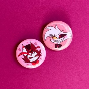 Può includere: Due bottoni rotondi rosa con personaggi dei cartoni animati. Il primo bottone presenta un gatto bianco con occhi rossi e un papillon nero. Il secondo bottone presenta un gatto rosso con un cappello a cilindro nero e un papillon rosso. Entrambi i bottoni hanno uno sfondo rosa con cuori bianchi.