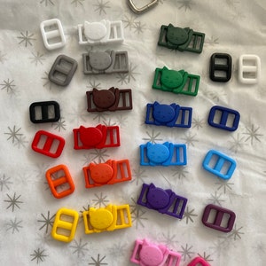May include: Assortment of colorful plastic cat-shaped slider buckles with matching rectangular slider buckles in various colors, including white, gray, brown, green, blue, purple, orange, yellow, and pink.