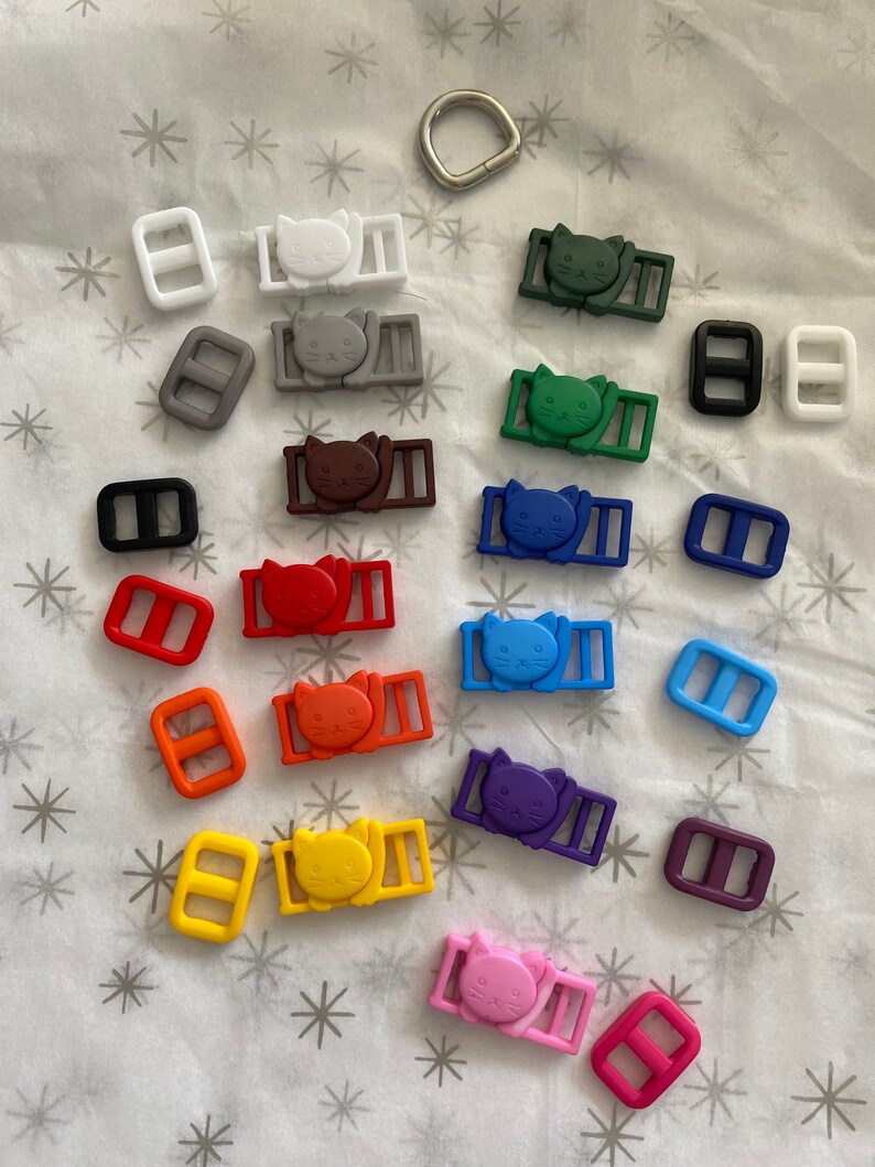 May include: Assortment of colorful plastic cat-shaped slider buckles with matching rectangular slider buckles in various colors, including white, gray, brown, green, blue, purple, orange, yellow, and pink.
