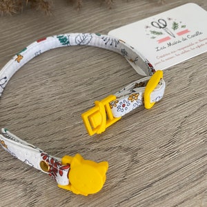 May include: A white and yellow cat collar with a floral pattern and a yellow cat-shaped buckle. The collar is made by Les Mains de Camille, a company that creates eco-responsible products for the home.