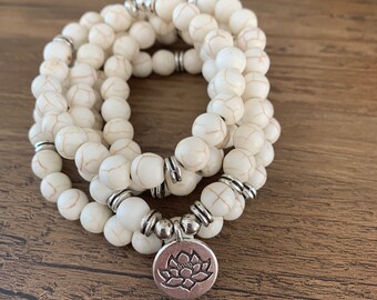 May include: White beaded bracelet with a silver lotus charm. The bracelet is made of multiple strands of small, round beads.
