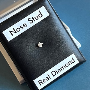 May include: A small, clear diamond nose stud in a black velvet box with the words "Nose Stud" and "Real Diamond" printed on the box.